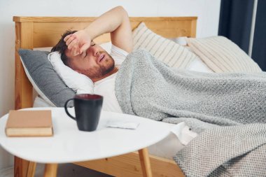 Hasta adam evde yatağa uzanmış ve kendini kötü hissediyor. Kişisel izolasyon kavramı.