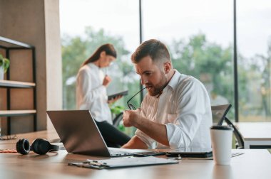 Masanın yanında oturan beyaz kadın arka planda. Çalışanlar modern ofiste birlikte çalışıyorlar..