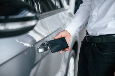 Elinde akıllı telefonla. Beyaz elbiseli genç adam araba galerisinde..