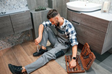 Ekipman çantasıyla birlikte yerde. Üniformalı tesisatçı evde..