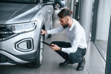 Tekerlekleri kontrol ediyorum. Beyaz elbiseli genç adam araba galerisinde..