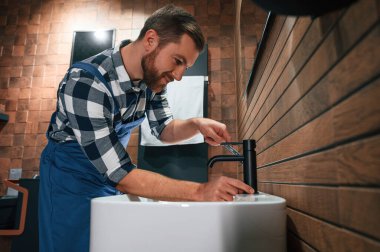 Lavabo ve musluğu tamir ediyorum. Mavi üniformalı tesisatçı banyoda çalışıyor..