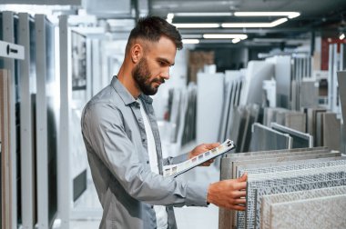 Elinde not defteriyle dikiliyorsun. Tarz sahibi güzel adam ev için malzeme deposunda..