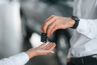 Yeni otomobilin anahtarlarını vermek. Beyaz elbiseli bir adam araba galerisinde birlikte..