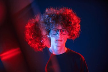 Sol tarafta cam yansıması. Kıvırcık saçlı genç adam kapalı alanda neon ışıkla aydınlatılır..