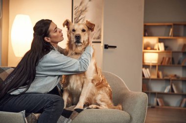 Oynuyor ve kanepede oturuyordu. Kadın Golden Retriever köpeğiyle evde..