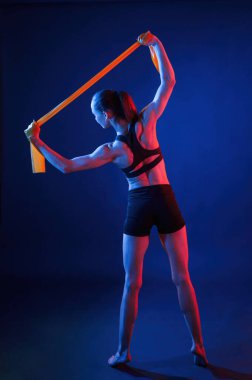 Ellerini uzatmak için sarı renkli bant. Güzel kaslı kadın stüdyoda neon ışıklı..