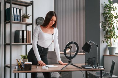 Akıllı telefon kürsüde, kaydediyor. Beyaz elbiseli genç ve güzel bayan ofiste..