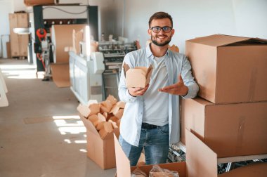 Tahta çarşafları tutuyor ve gösteriyor. Beyaz elbiseli matbaacı içeride..