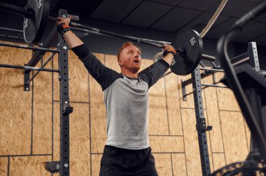 Ellerin havada durarak. Güçlü adam spor salonunda halteri kaldırıyor..