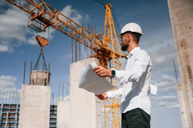 Planı ellerindeyken. Üniformalı adam inşaat alanında çalışıyor..