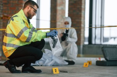 Kadın fotoğraf makinesi kullanıyor, fotoğraf çekiyor. Dedektifler cesedin yanındaki suç mahallinde kanıt topluyorlar..