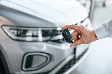 Anahtarlar ve uzaktan kumanda. Manzarayı kapat. Beyaz elbiseli genç adam araba galerisinde..