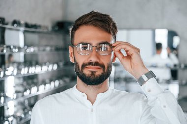 Modern görünüş. Optik mağazasından gözlük seçen sakallı şık bir adam..