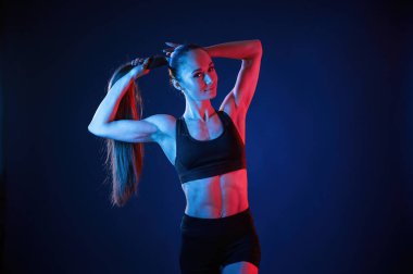 Saçını düzeltiyor. Güzel kaslı kadın stüdyoda neon ışıklı..