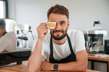 Fincan ile eğleniyorum. Beyaz gömlekli ve siyah önlüklü kafe çalışanı içeride..