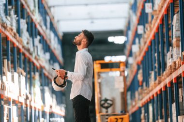 Elinde tabletle. Depo işçisi depoda bir sürü ürünle birlikte..