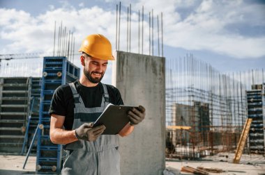 Sürecin kontrolü. Foreman belgelerle birlikte. Üniformalı adam inşaat alanında çalışıyor..