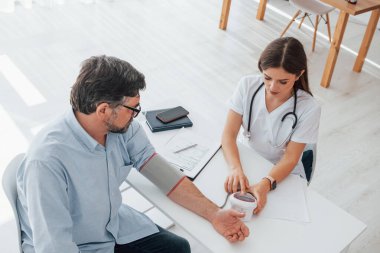 Kan basıncını ölçüp belgeyi kontrol ediyorum. Ofiste beyaz önlüklü profesyonel bir sağlık görevlisi var..