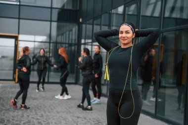 Sarı renkli atlama ipiyle. Bir grup sportif kadın dışarıda, siyah binanın yakınında..