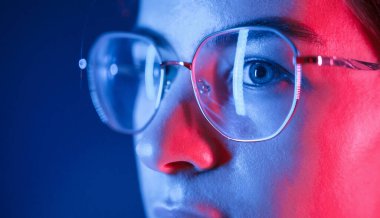 Gözlüklü. Manzarayı kapat. Stüdyoda neon ışıkla aydınlatılmış genç ve güzel bir kadın var..