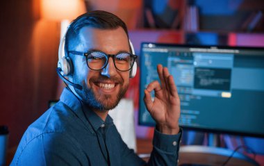 Oturuyor ve gülümsüyor. Profesyonel programcı içeride çalışıyor. Neon ışıkları.