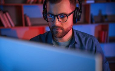 Ön manzara. Evdeki bilgisayar başında oturan bir adam. Neon ışıkları.