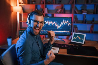 Happy borsa simsarı içeride bilgisayar başında çalışıyor ve başarıyı kutluyor. Değişim ve para kavramı.