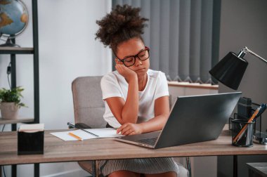 Sıkıldım. Şirin Afrikalı Amerikalı kız öğrenci dizüstü bilgisayarın yanında oturuyor..