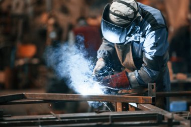 Manzarayı kapat. Koruyucu maskeli fabrika işçisi demiri kaynaklıyor..