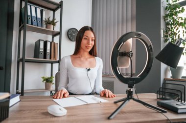 Profesyonel ışıklandırma. Çevrimiçi ana sınıf. Beyaz elbiseli genç ve güzel bayan ofiste..