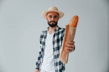 Şapkalı turist elinde baget ekmeği tutuyor. Yakışıklı adam stüdyoda beyaz arka plana karşı..