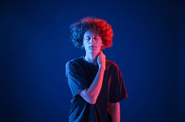 Kameraya poz veriyorum. Kıvırcık saçlı genç adam kapalı alanda neon ışıkla aydınlatılır..