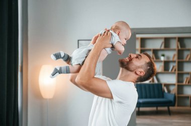 Gülümsemek, bebekle eğlenmek ellerimizde. Bebekli baba evde, oğluyla ilgileniyor..