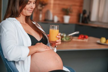 Göbeğe dokunmak ve portakal suyuyla bardağı tutmak. Güzel hamile kadın evde..