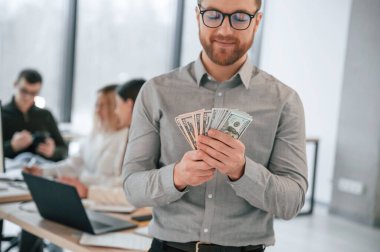 Adam parayı elinde tutuyor. Ofiste başarılı bir ekip birlikte çalışıyor. İş kavramı.