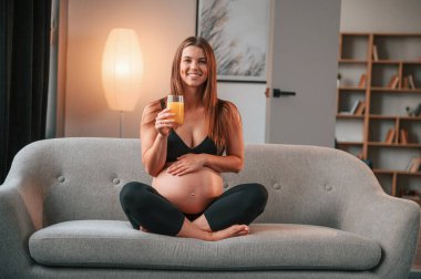 Kanepede oturup portakal suyu içmek. Güzel hamile kadın evde..