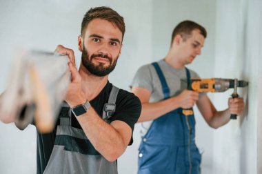 İnşaat parçalarını elle taşımak. Matkabı kullanarak. İki adam dairede birlikte tamirat yapıyor..