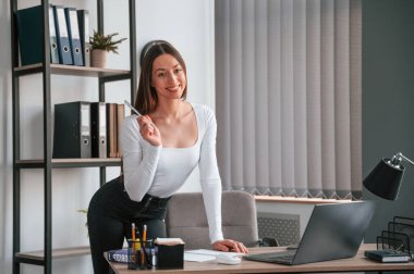 Masanın yanında duruyor. Beyaz elbiseli genç ve güzel bayan ofiste..