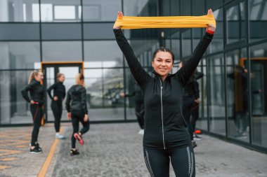 Genişletici tutuluyor. Bir grup sportif kadın dışarıda, siyah binanın yakınında..