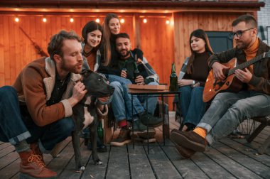 Bir grup insan akşam vakti güzel ahşap binanın yanında toplanıyor..
