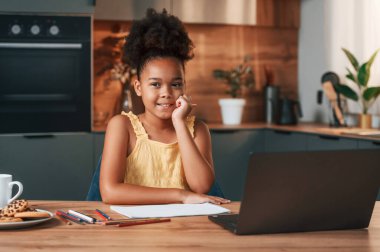 Çizim için dizüstü bilgisayar ve kağıtla. Gündüz vakti evde rahat giyinen sevimli siyah kız var..