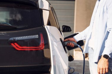 Şarj aleti takıldı. Elektrikli arabasıyla adamın yakın görüntüsü.
