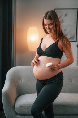 Karnı kremalı. Kalp şeklinde. Güzel hamile kadın evde..