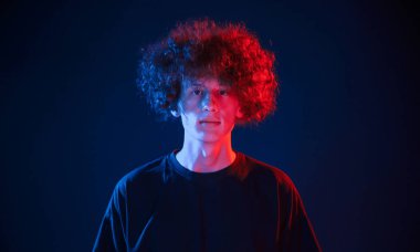 Kapalı alanda duran kıvırcık saçlı genç adam portresi, neon ışıkla aydınlatılmış..