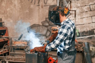 Koruyucu maskeli. Ütüyü kaynaklıyorum. Üniformalı fabrika çalışanı içeride..