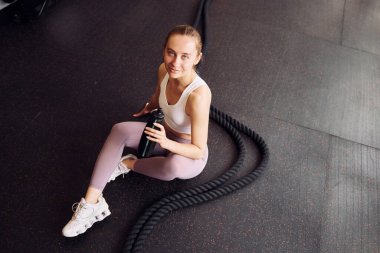 Üst Manzara. Oturup ara veriyoruz. Spor elbiseli genç bir kadın spor salonunda spor yapıyor..