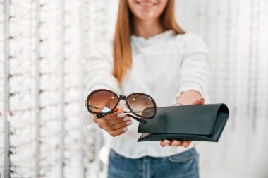 Kahverengi lensler ve siyah çanta. Mağazada elinde bardak tutan bir kadın. Görüntüyü kapat.