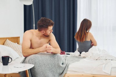 Hayal kırıklığına uğramış bir kadın kendini kötü hisseden bir adamla yatakta oturuyor..