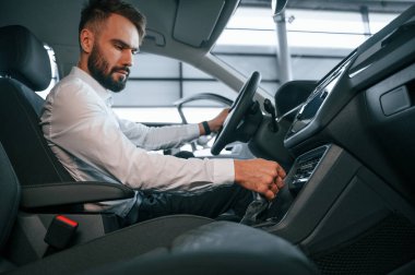 Yan görüş. Bir otomobilin içinde oturuyor. Beyaz elbiseli genç adam araba galerisinde..